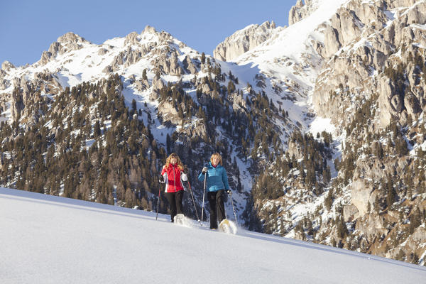 two models are walking with snowshoes on fresh snow feeling the emotion of the powder, Villnöss, Bolzano province, South Tyrol, Trentino Alto Adige, Italy, Europe