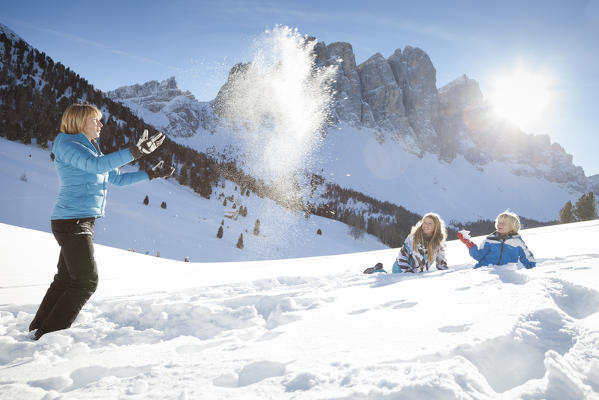 a happy family is playing with the snow in a peaceful sunny day with Geisler in the background, Villnöss, Bolzano province, South Tyrol, Trentino Alto Adige, Italy, Europe