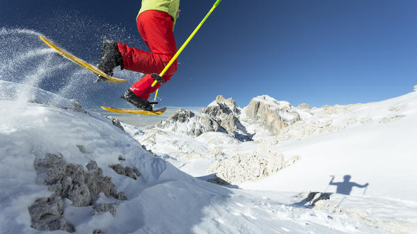 a trekker with yellow snowshoes jumping off the boulder with the Pala Group in the background, Trento province, Trentino Alto Adige, Italy, Europe,