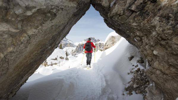 a suggestive view of a hiker with snowshoes seen through a natural tunnel in the rocks, Belluno province, Veneto, Italy, Europe,