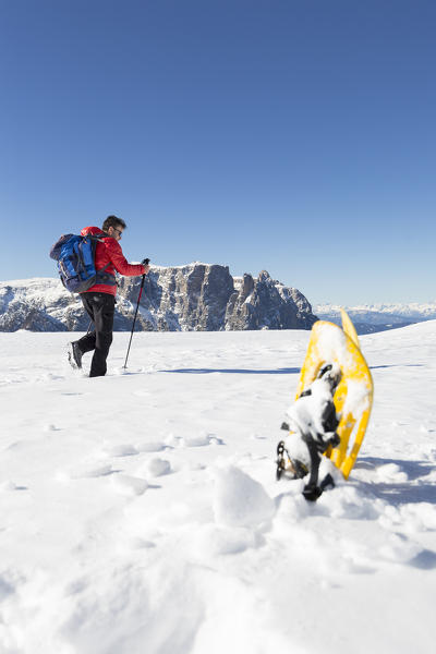 a view of a hiker walking into fresh snow with a pair of yellow snowshoes in the foreground and the Schlern in the background, Bolzano province, South Tyrol, Trentino Alto Adige, Italy, Europe