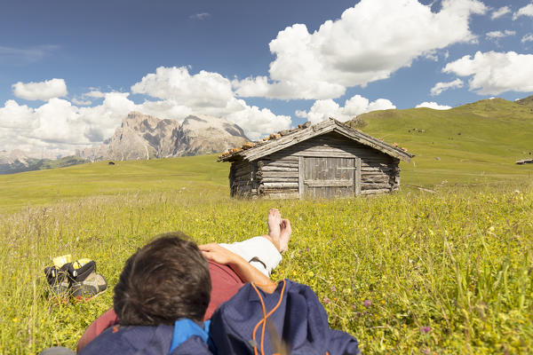a hiker is relaxing on a meadow on the Seiser Alm, with a beautiful view on the Dolomites, Bolzano province, South Tyrol, Trentino Alto Adige, Italy