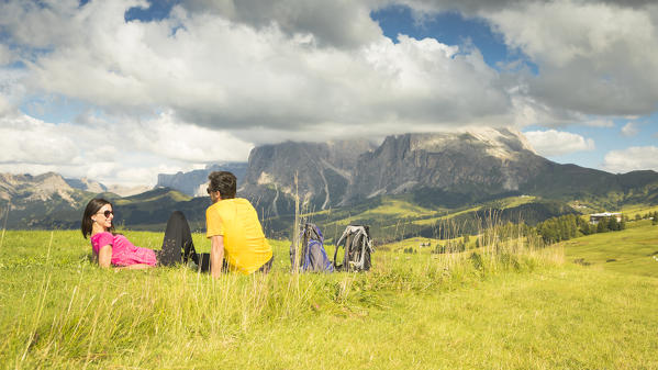 a couple is sitting and relaxing on a meadow on the Seiser alm, (Alpe di Siusi), Bolzano province, South Tyrol, Trentino Alto Adige, Italy