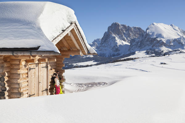 a couple of skiers are relaxing under the sun on the Seiser Alm with the Langkofel Group in the background, Bolzano province, South Tyrol, Trentino Alto Adige, Italy