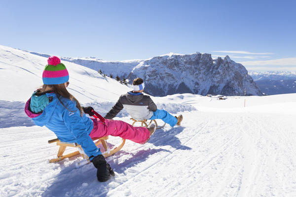 two tourists are going down with a sled on the Seiser Alm with the Schlern in the background, Bolzano province, South Tyrol, Trentino Alto Adige, Italy