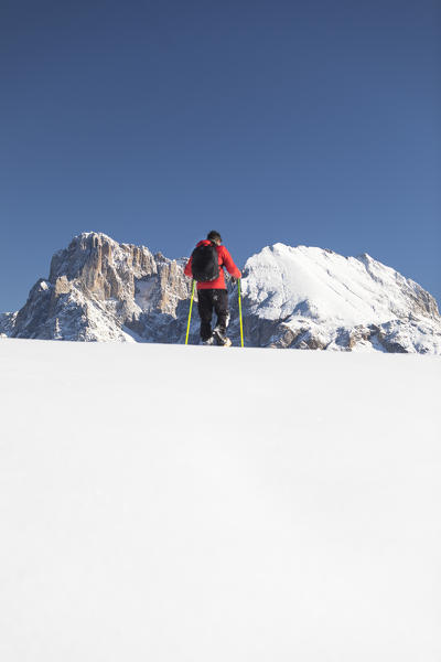 a hiker is trekking with snowshoes on the Seiseralm with Langkofel and Plattkofel in the background, Bolzano province, South Tyrol, Trentino Alto Adige, Italy