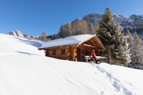 a hiker is relaxing on the snow in front of a mountain hut in Val Gardena, Bolzano province, South Tyrol, Trentino Alto Adige, Italy