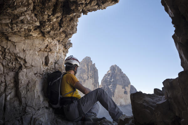 a hiker is sitting at a natural window along the Paternkofel tunnel and staring at the Three Peaks of Lavaredo,  bolzano province, south tyrol, trentino alto adige, italy,