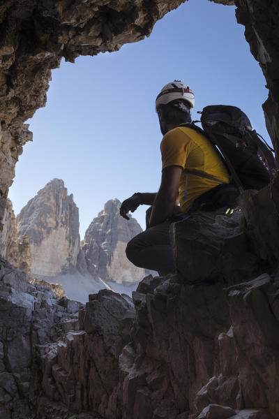 a hiker is sitting at a natural window along the Paternkofel tunnel and staring at the Three Peaks of Lavaredo,  bolzano province, south tyrol, trentino alto adige, italy,