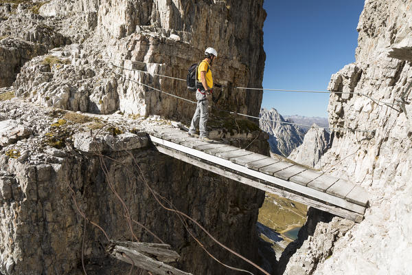a hiker is passing on a little wood bridge along the Peace Way (Via della Pace), into the Sextner Dolomites,  bolzano province, south tyrol, trentino alto adige, italy,