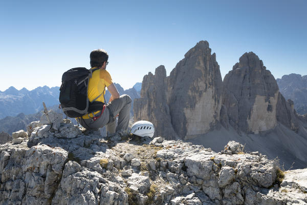 a hiker is sitting on the top of the Paternkofel, staring at the Three Peaks of Lavaredo, sextner Dolomites,  bolzano province, south tyrol, trentino alto adige, italy,