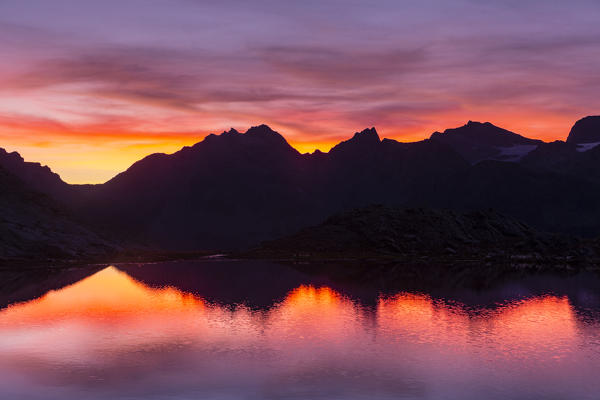 Sunsetscape of mountains reflected in an alpine lake during a summer sunset. Confinale pass lake, Valmalenco valley, Sondrio district, Valtellina, Alps, Lombardy, Italy, Europe. 