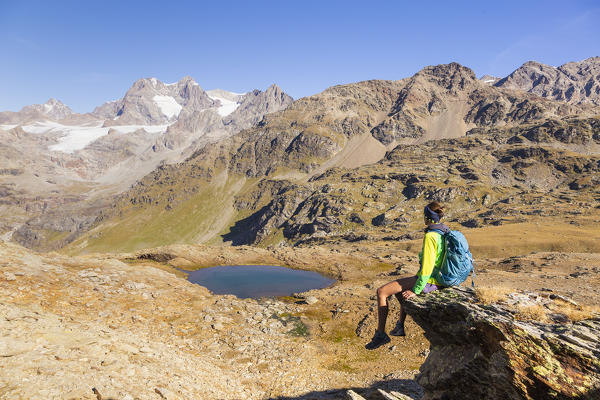 Hiker looking to the mountainscape during summer in italian Alps. Confinale pass lake, Valmalenco valley, Sondrio district, Valtellina, Alps, Lombardy, Italy, Europe.