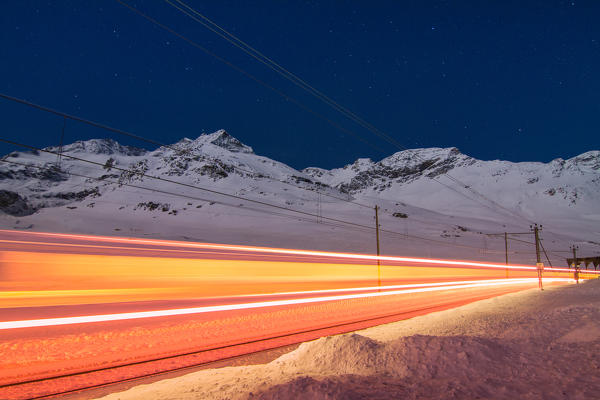 Red train at Berninapass in a full moon winter night