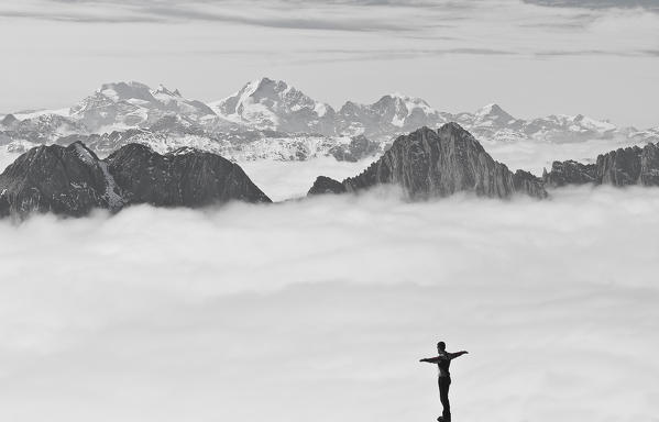 Trekker on a summit over a sea of clouds in high Valtellina valley, Sondrio province, Lombardy, Italy