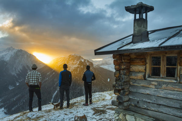 Three friends admiring sunrise from an alpine hut. Livigno, Valtellina, Italy
