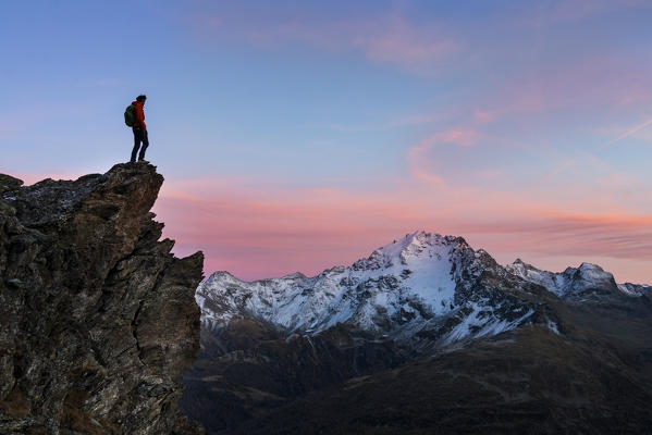 An hiker on a rock in Viola valley with a panoramic view at sunset. Valdidentro, Valtellina, Lombardy, Italy