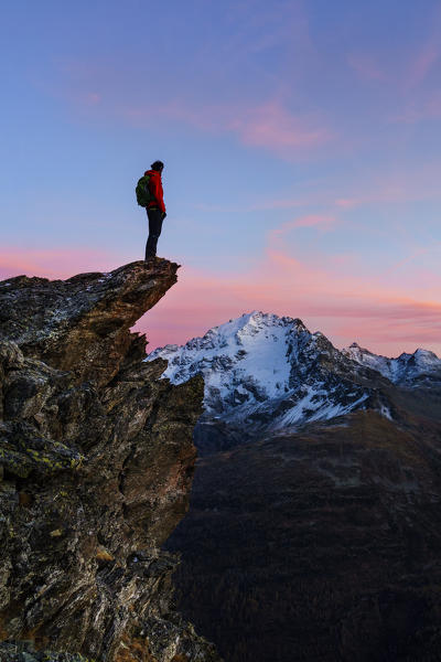An hiker on a rock with a panoramic view at sunset. Valdidentro, Valtellina, Lombardy, Italy