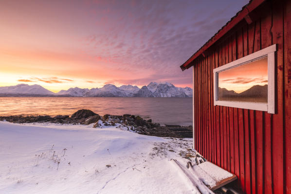 The sunset reflected on the glass of a typical red house. Nordmannvik, Kafjord, Lyngen Alps, Troms, Norway, Lapland, Europe.