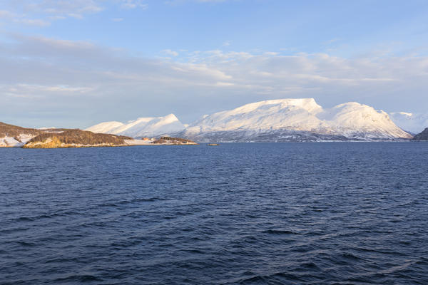 The sun illuminates the peaks overlooking the fjord. Lyngenfjord, Lyngen Alps, Troms, Norway, Lapland, Europe.
