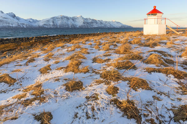 The sun illuminates the coast near a traditional lighthouse. Spaknesora naturreservat, Djupvik, Lyngenfjord, Lyngen Alps, Troms, Norway, Lapland, Europe.