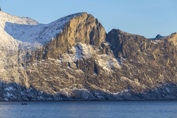 Fishing boat sails in Mefjorden with imposing rock walls behind it. Mefjordvaer, Mefjorden, Senja, Norway, Europe.