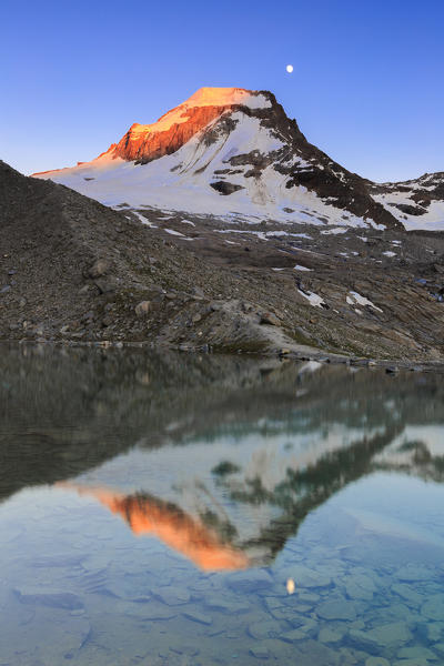 Ciarforon still illuminated by the colors of dawn and the moon are reflected in Moncorvè lake. Valsavarance, Gran Paradiso National Park, Aosta Valley, Italy, Europe