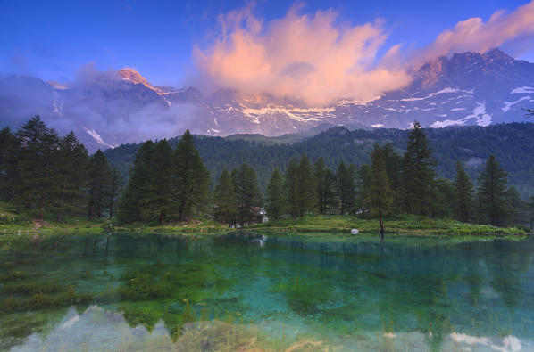 Cloud illuminated by the colors of dawn is reflected in Blue Lake. Blu Lake, Cervinia, Valtournanche, Aosta valley, Italy, Europe