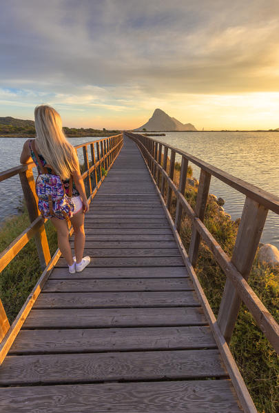 A girl looks sunrise from a pedestrian walkway. Porto Taverna, Loiri Porto San Paolo, Olbia Tempio province, Sardinia, Italy, Europe.