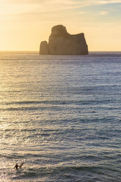 A surfer looks the rock of Pan di Zucchero at sunset. Beach of Masua, Iglesias, Sud Sardegna province, Sardinia, Italy, Europe.