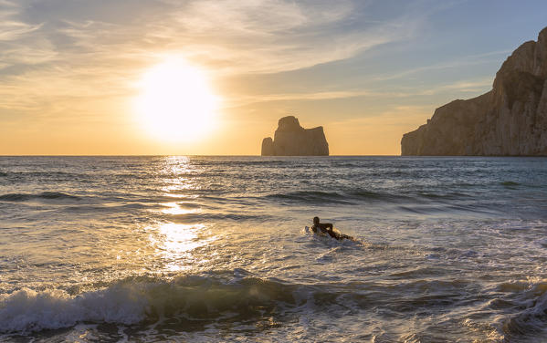 A surfer swims at sunset.  Beach of Masua, Iglesias, Sud Sardegna province, Sardinia, Italy, Europe.