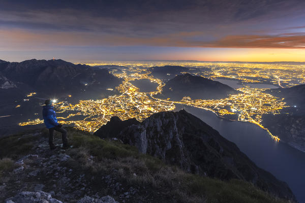 Hiker admire lights of Lecco city from the top of Coltignone mount, Lecco province, Lombardy, Italy, Europe (MR)
