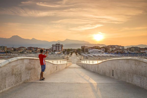 A tourist take a photo at sunrise on Lido di Camaiore pier, Lucca province, Versilia, Tuscany, Italy, Europe