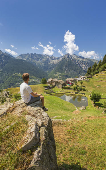 Hiker relax looking at the Lagunc village, San Giacomo Filippo, Chiavenna valley, Sondrio province, Lombardy, Italy, Europe (MR)
