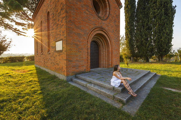 Girl take a relax at the red church of Pomelasca at sunset, Inverigo, Como province, Brianza, Lombardy, Italy, Europe (MR)