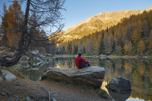 Hiker take relax and looks at the autumn reflections on Azzurro lake, Motta, Campodolcino, Sondrio province, Lombardy, Italy, Europe (MR)