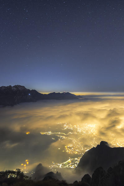 A night view of Lecco city wrapped of clouds from the top of Coltignone mount, Piani dei Resinelli, Lecco province, Lombardy, Italy, Europe