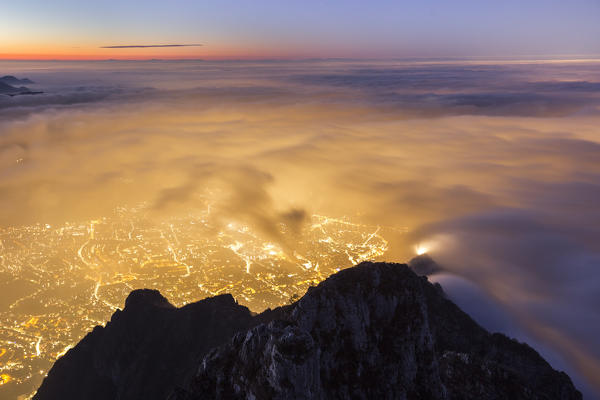 A dawn view of Lecco city wrapped of clouds from the top of Coltignone mount, Piani dei Resinelli, Lecco province, Lombardy, Italy, Europe