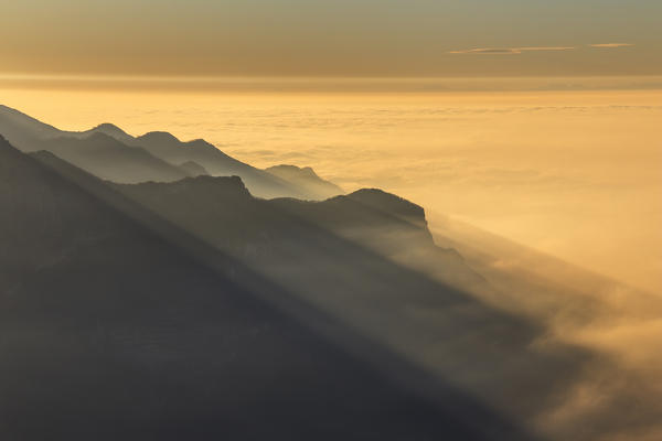First rays of the sunrise on Lecco mountains peaks above the clouds, view from the top of Coltignone mount, Piani dei Resinelli, Lecco province, Lombardy, Italy, Europe