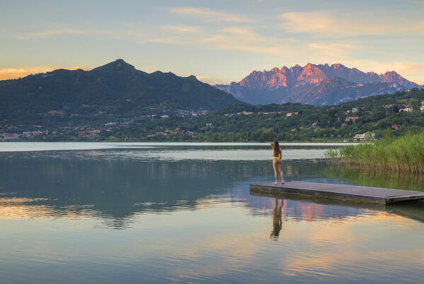 Girl relaxes and looks sunset on Lecco mountains (Resegone and Barro mount) reflected into the Oggiono lake in summertime, Annone lake, Oggiono, Brianza, Lecco province, Lombardy, Italy, Europe (MR)