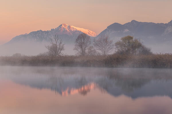 Foggy sunrise on Grigna Meridionale (Grignetta) reflected into the Adda river, Airuno, Lecco province, Lombardy, Italy, Europe