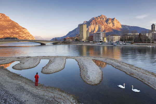 Man looks Lecco city and Coltignone mount at sunrise from Malgrate riverfront, Adda river, lake Como, Lecco province, Lombardy, Italy, Europe (MR)