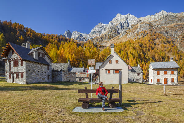 Hiker take a relax sitting on a bench of Pedemonte village in autumnal time, Alpe Devero, Baceno, Alpe Veglia and Alpe Devero natural park, province of Verbano-Cusio-Ossola, Piedmont, italy, Europe (MR)