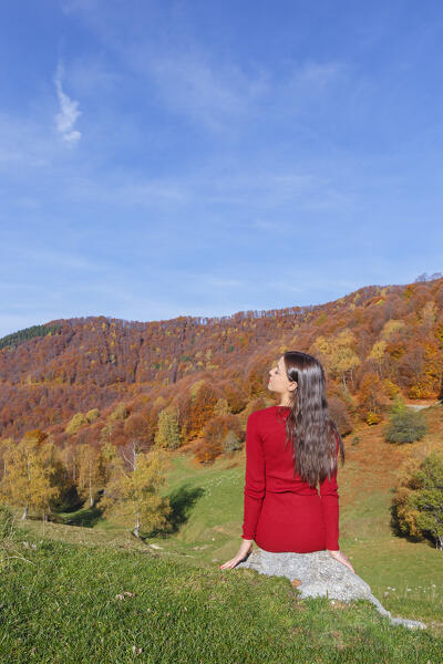 Girl in a red dress relaxes on meadow near the autumn forest, Tremezzina, Intelvi valley (val d'Intelvi), Como province, Lombardy, Italy, Europe (MR)