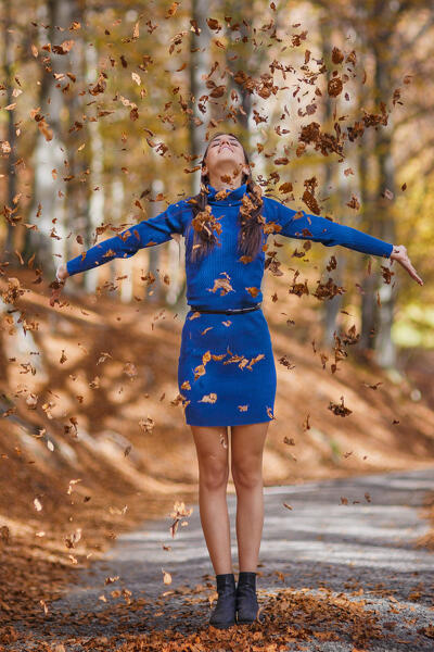 A portrait of young woman in a blue dress while playing throwing autumn leaves in the forest, Ponna Superiore, Intelvi valley (val d'Intelvi), Como province, Lombardy, Italy, Europe (MR)