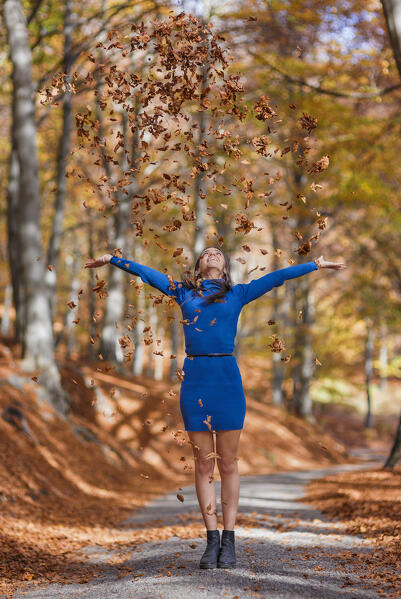 A portrait of young woman in a blue dress while playing throwing autumn leaves in the forest, Ponna Superiore, Intelvi valley (val d'Intelvi), Como province, Lombardy, Italy, Europe (MR)