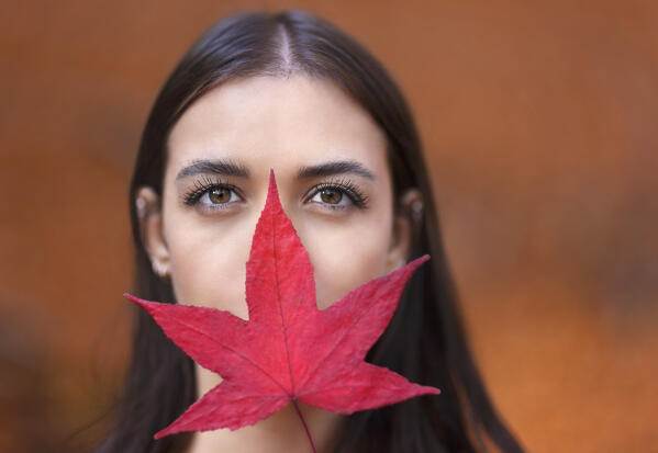 A portrait of a young woman with face cover up by a leaf of Liquidambar, Como province, Lombardy, Italy, Europe (MR)