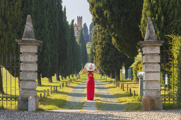 A young woman in red dress looks at the cypress avenue (Viale dei Cipressi), Brianza, Inverigo, Como province, Lombardy, Italy, Europe (MR)