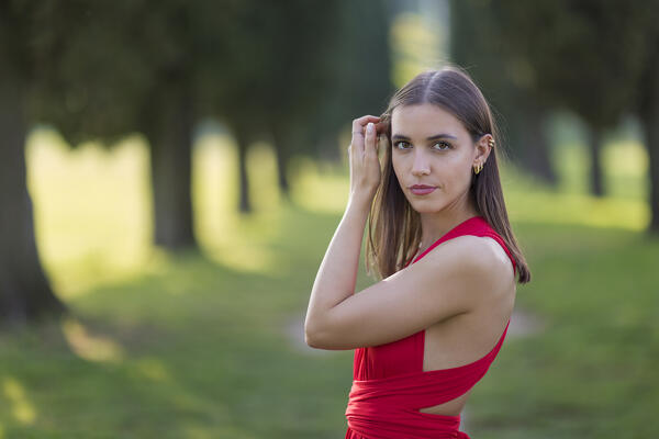 A portrait of a young woman in red dress on cypress avenue (Viale dei Cipressi), Brianza, Inverigo, Como province, Lombardy, Italy, Europe (MR)