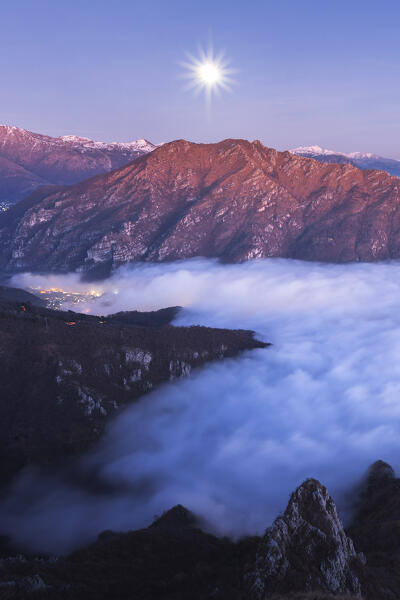 Dusk with full moon on Lecco and Valsassina wrapped up by the clouds, view from the top of Coltignone mount, lake Como, lecco province, Lombardy, Italy, Europe
